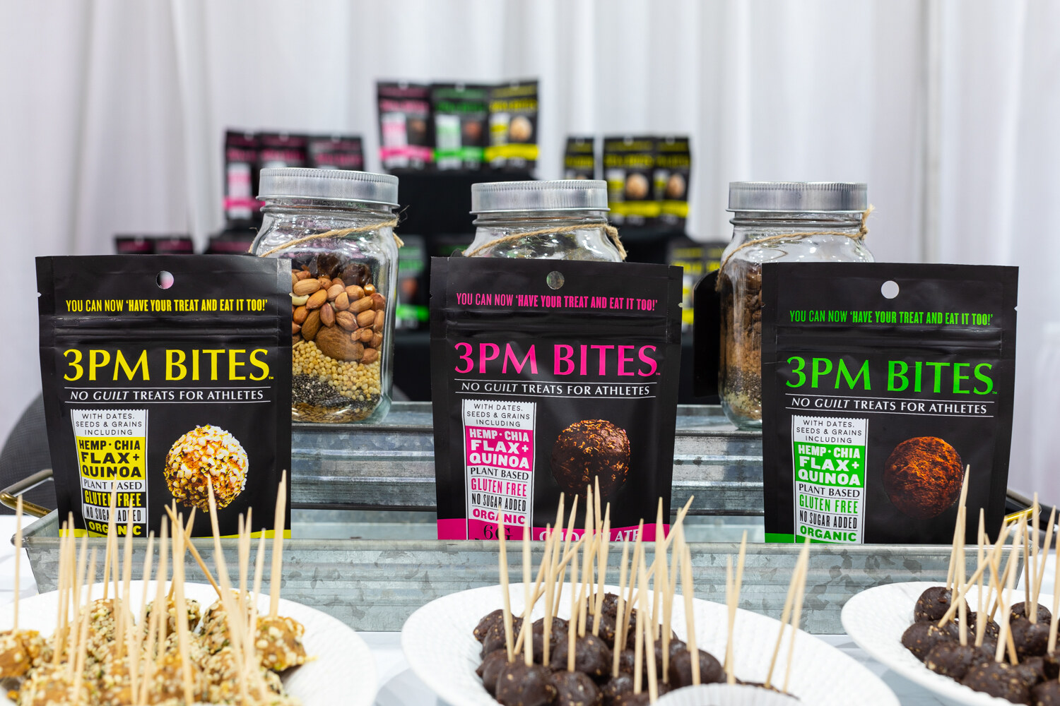 Black bags of 3PM Bites with sample plates of bites on toothpicks.