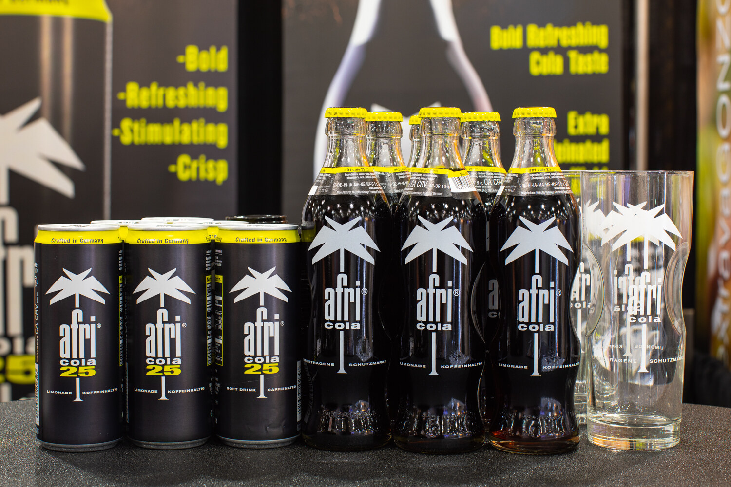 Cans and bottles of afri cola with a branded drinking glass.