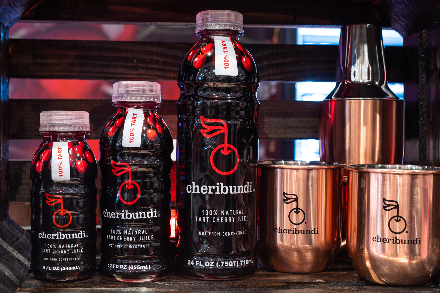 Three sizes of cheribundi bottles beside two copper mugs.