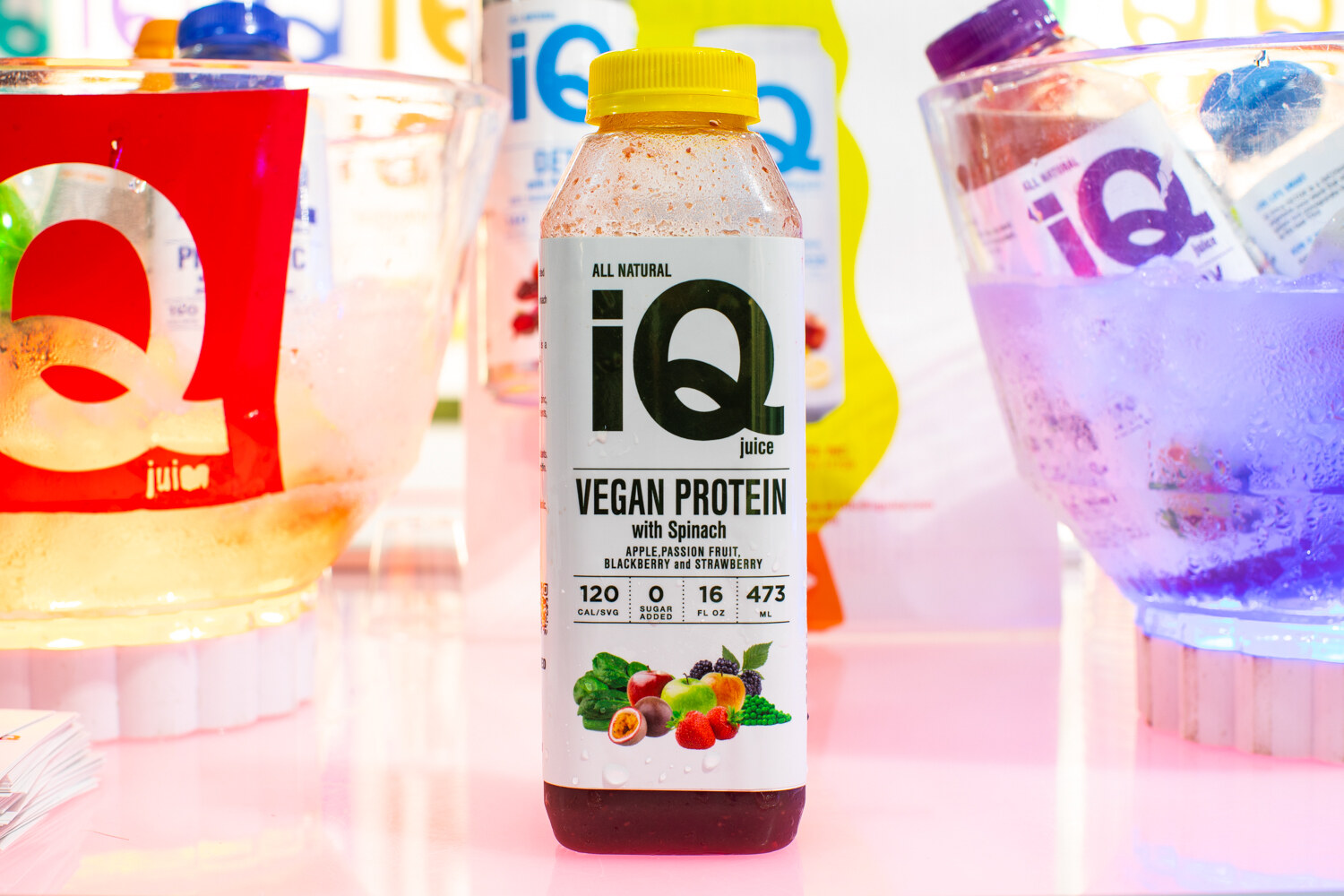 A bottle labeled iQ Vegan Protein with spinach in front of colorful lighting.