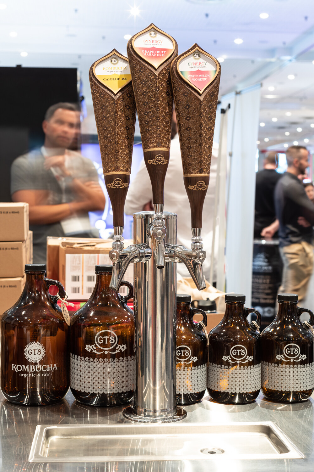 Three tall taps over brown glass growlers with a person behind.
