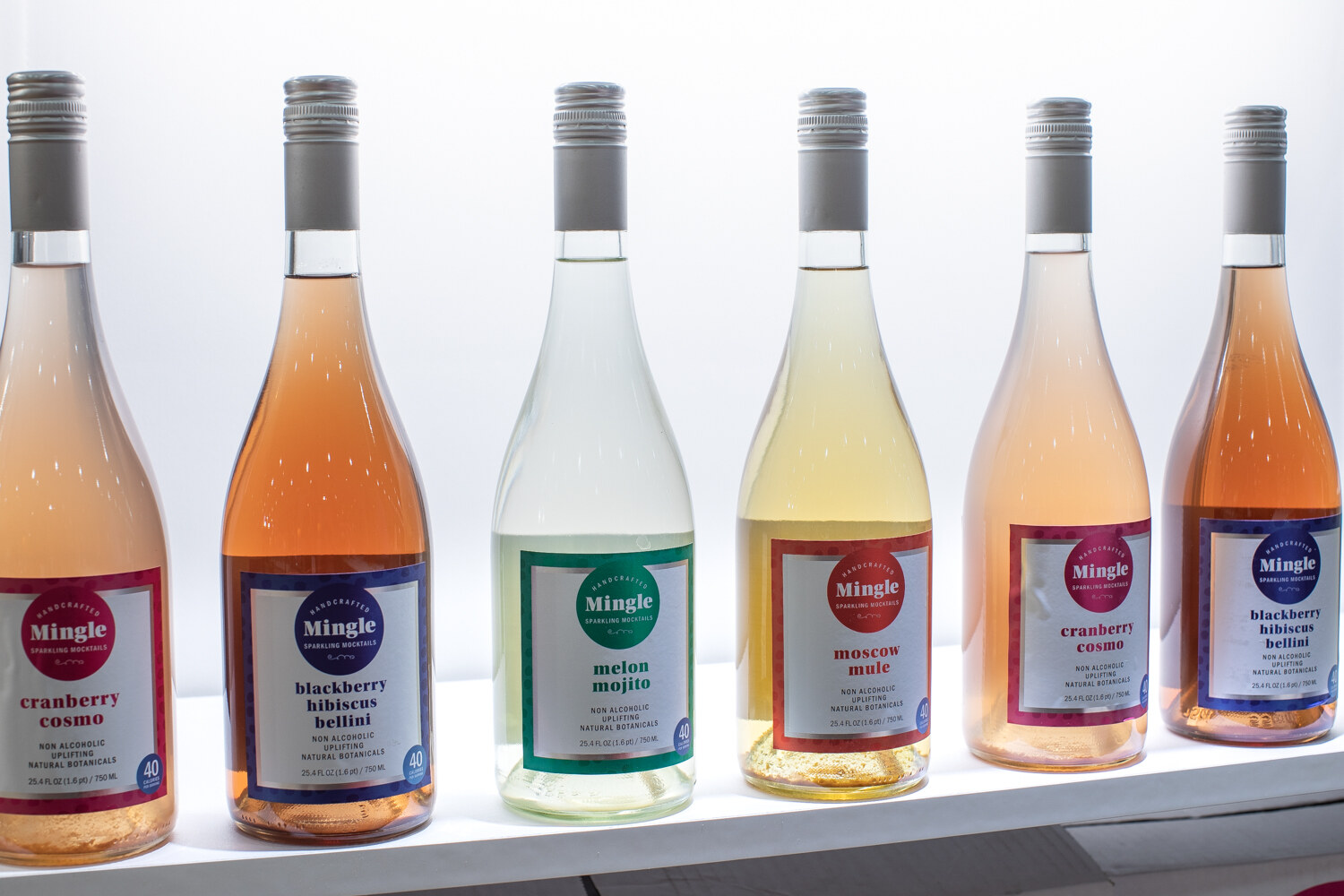 Six wine-style bottles with Mingle labels on a white shelf.