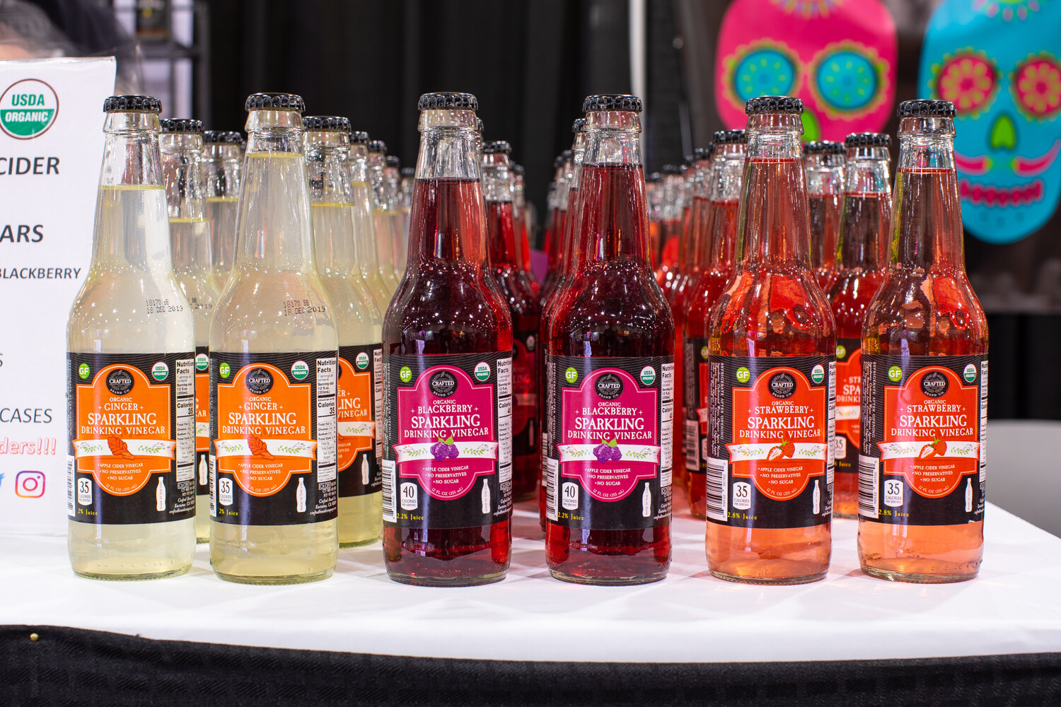 Many glass bottles of sparkling drinking vinegar in orange, pink and red labels.