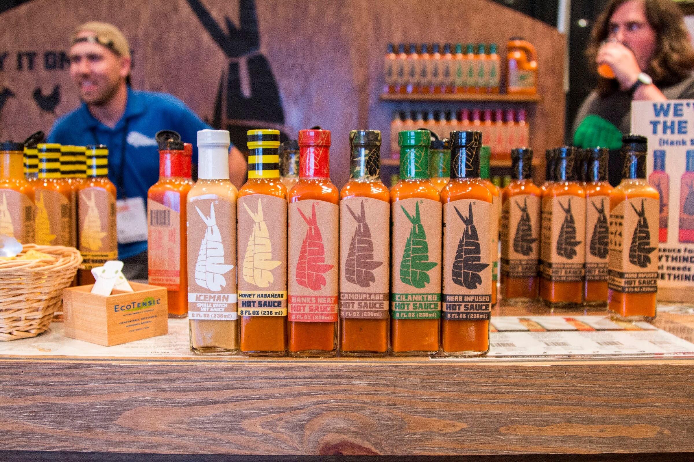 Photo of a row of hot sauce bottles with an exhibitor behind the table.