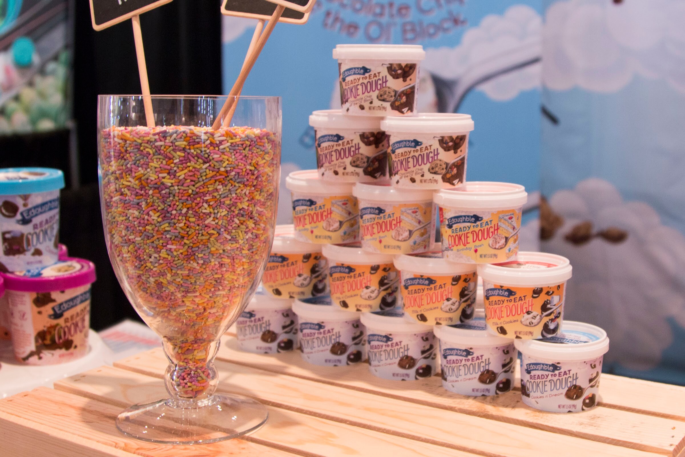 Photo of pints of cookie dough ice cream stacked beside a glass of rainbow sprinkles.