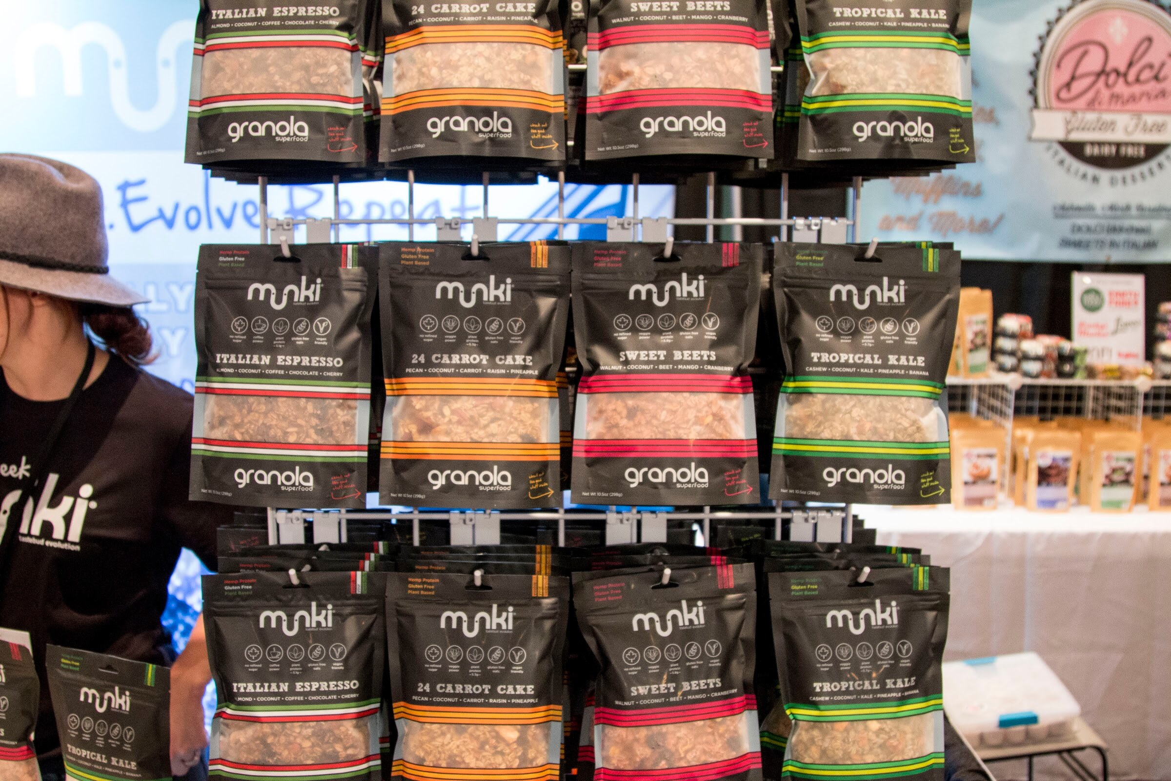 Photo of racks of munki granola bags beside a person in a black munki shirt.