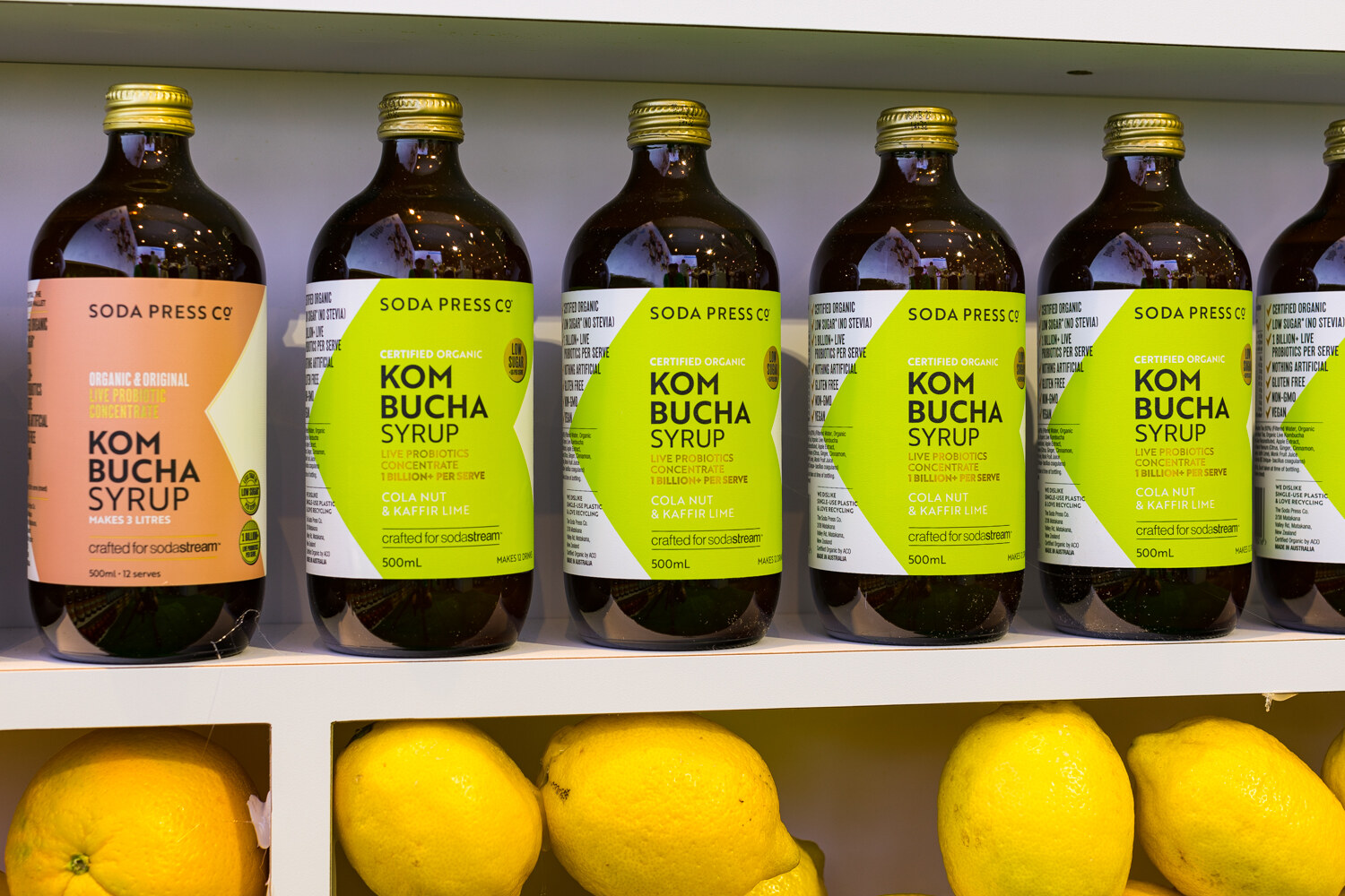 Photo of bottles of Kom Bucha Syrup on a shelf above a row of lemons.