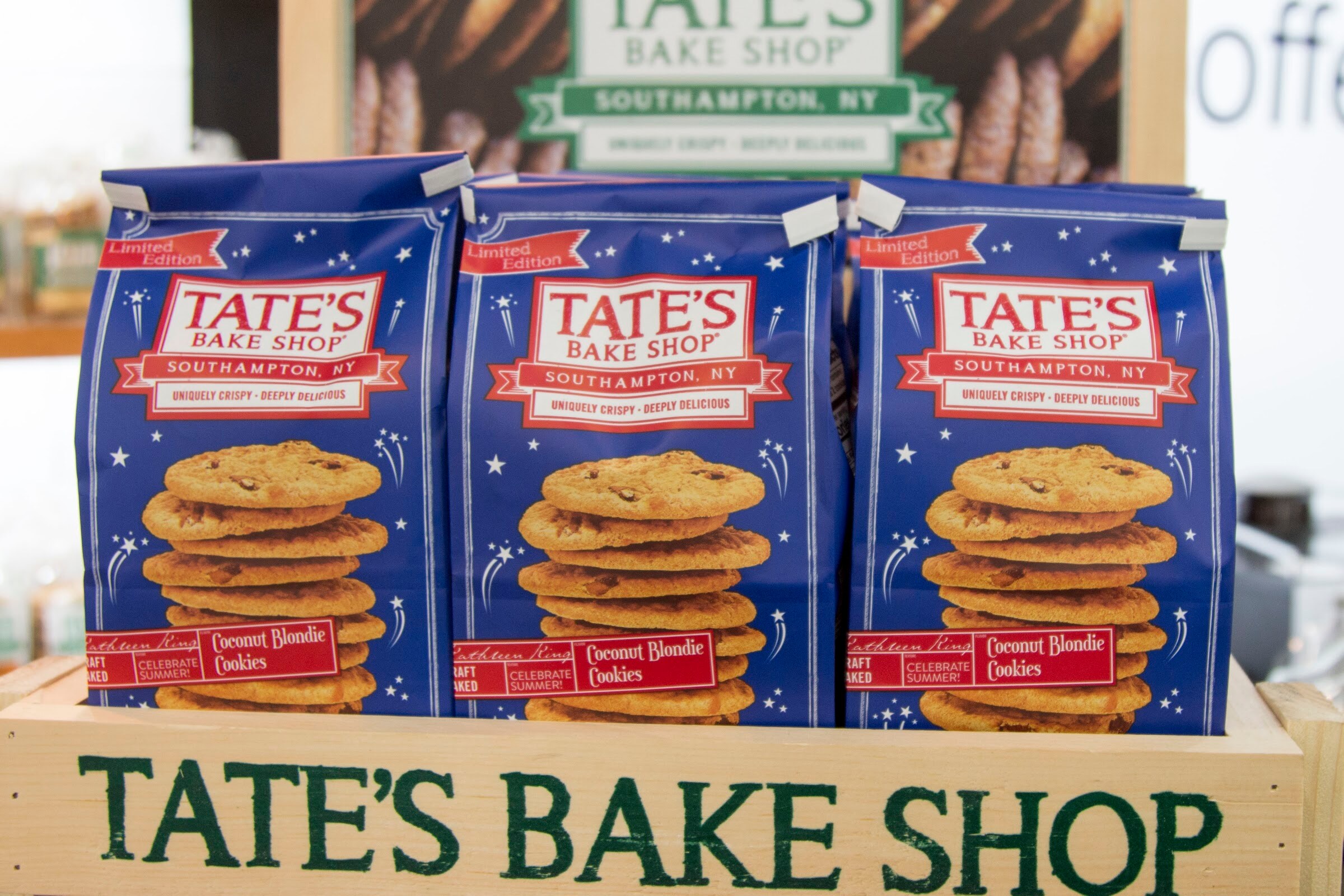 Photo of bags of Tate's Bake Shop coconut blondie cookies above a wooden Tate's sign.