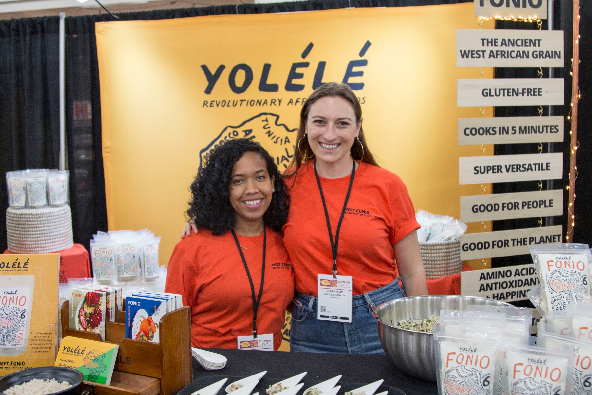 Photo of two women smiling in orange shirts at the Yolele booth.