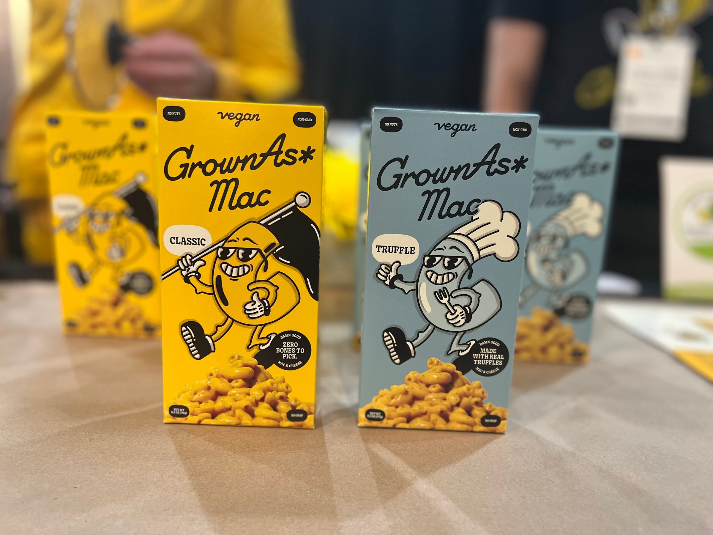 Yellow and blue GrownAs Mac vegan mac and cheese boxes in classic and truffle flavors stand on a table