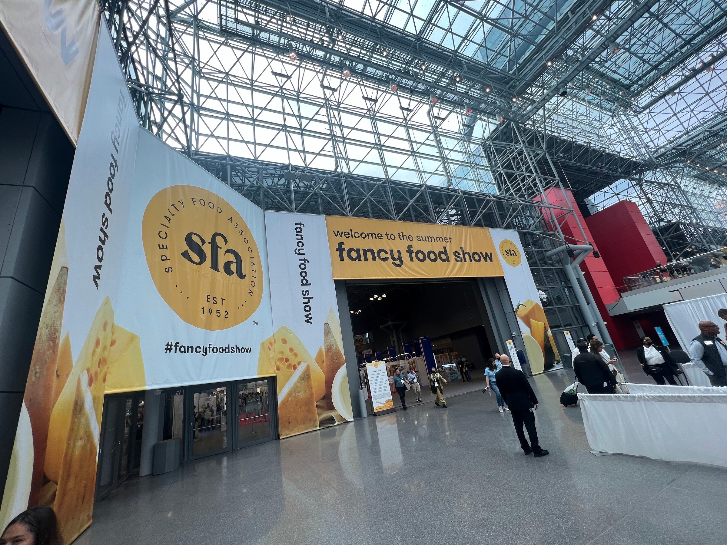 A large yellow and white welcome to the summer fancy food show banner with the Specialty Food Association logo arches over an entrance in the Javits Center