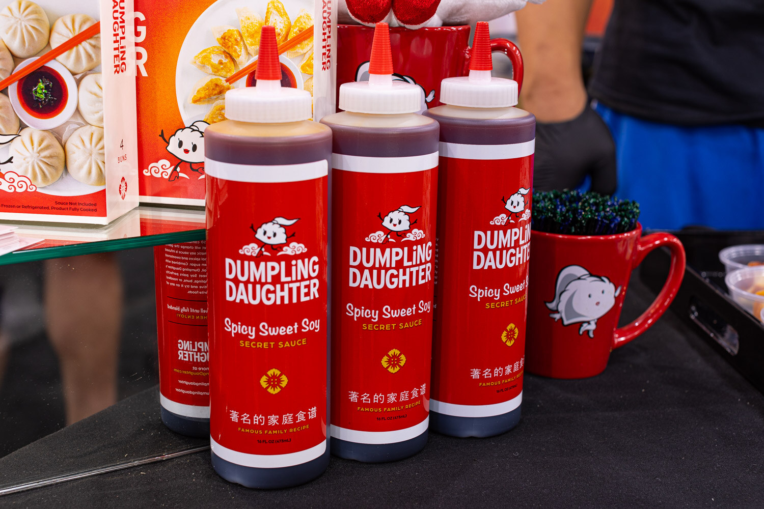 Three red Dumpling Daughter Spicy Sweet Soy squeeze bottles stand in front of a dumpling-themed display