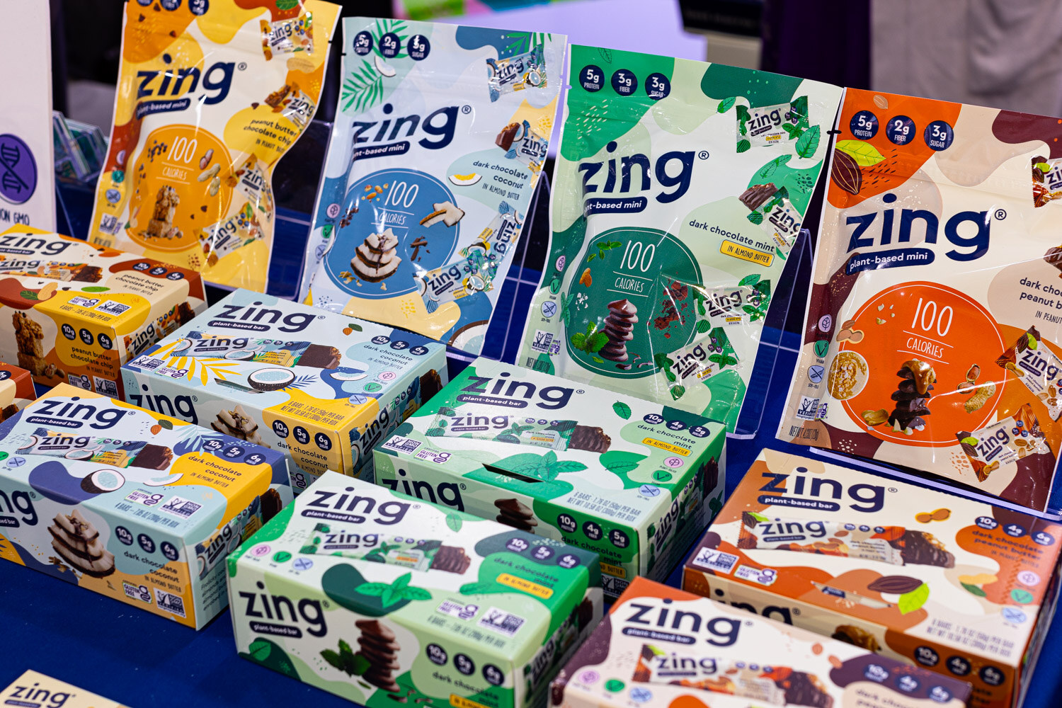 Boxes and bags of Zing snack bars in blue, green and yellow packaging are piled on a display