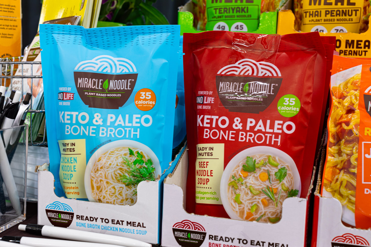 Blue and red Miracle Noodle Keto and Paleo Bone Broth noodle cups stand on a store-style display