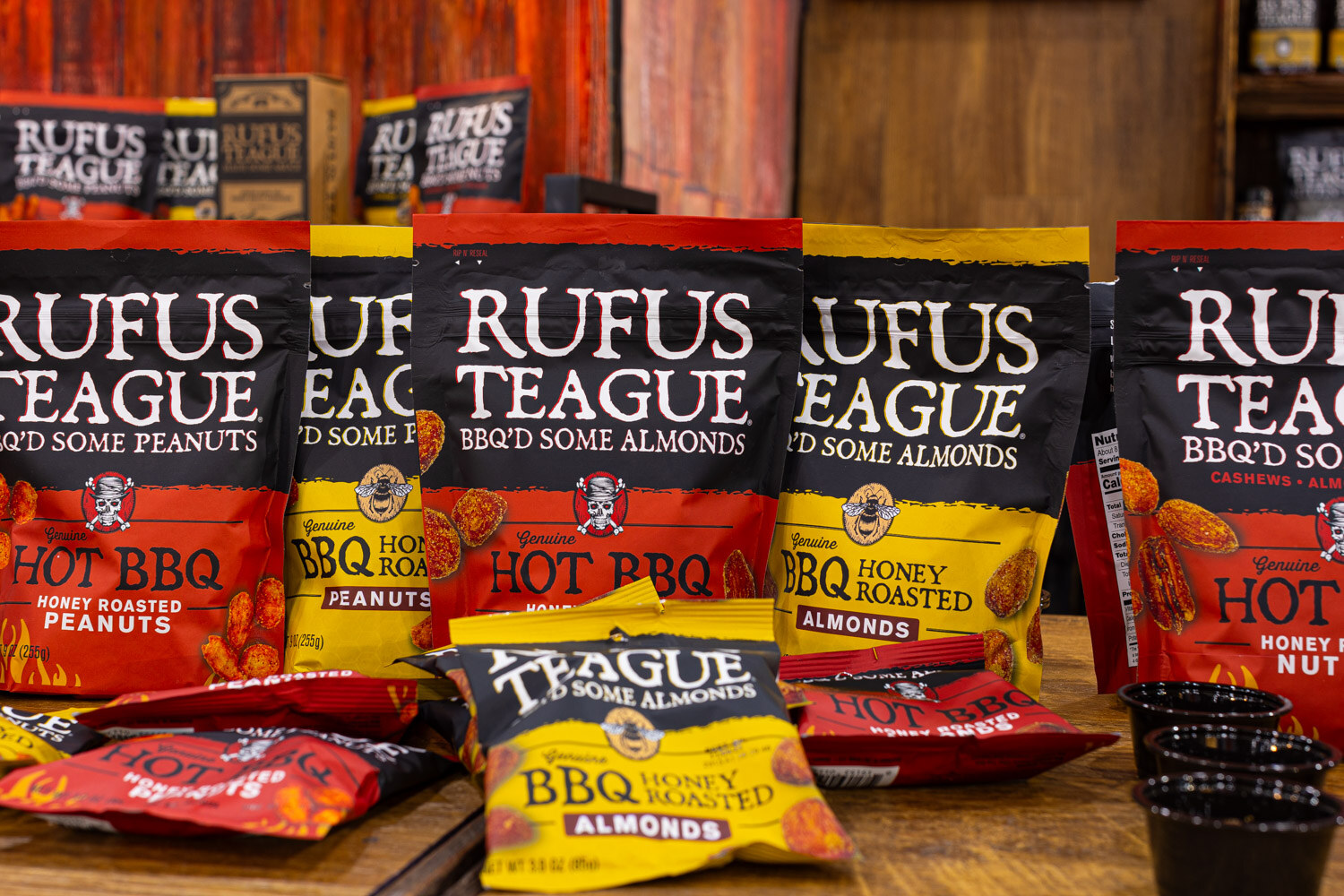 Bags of Rufus Teague BBQ and honey roasted peanuts and almonds sit on a rustic wooden display