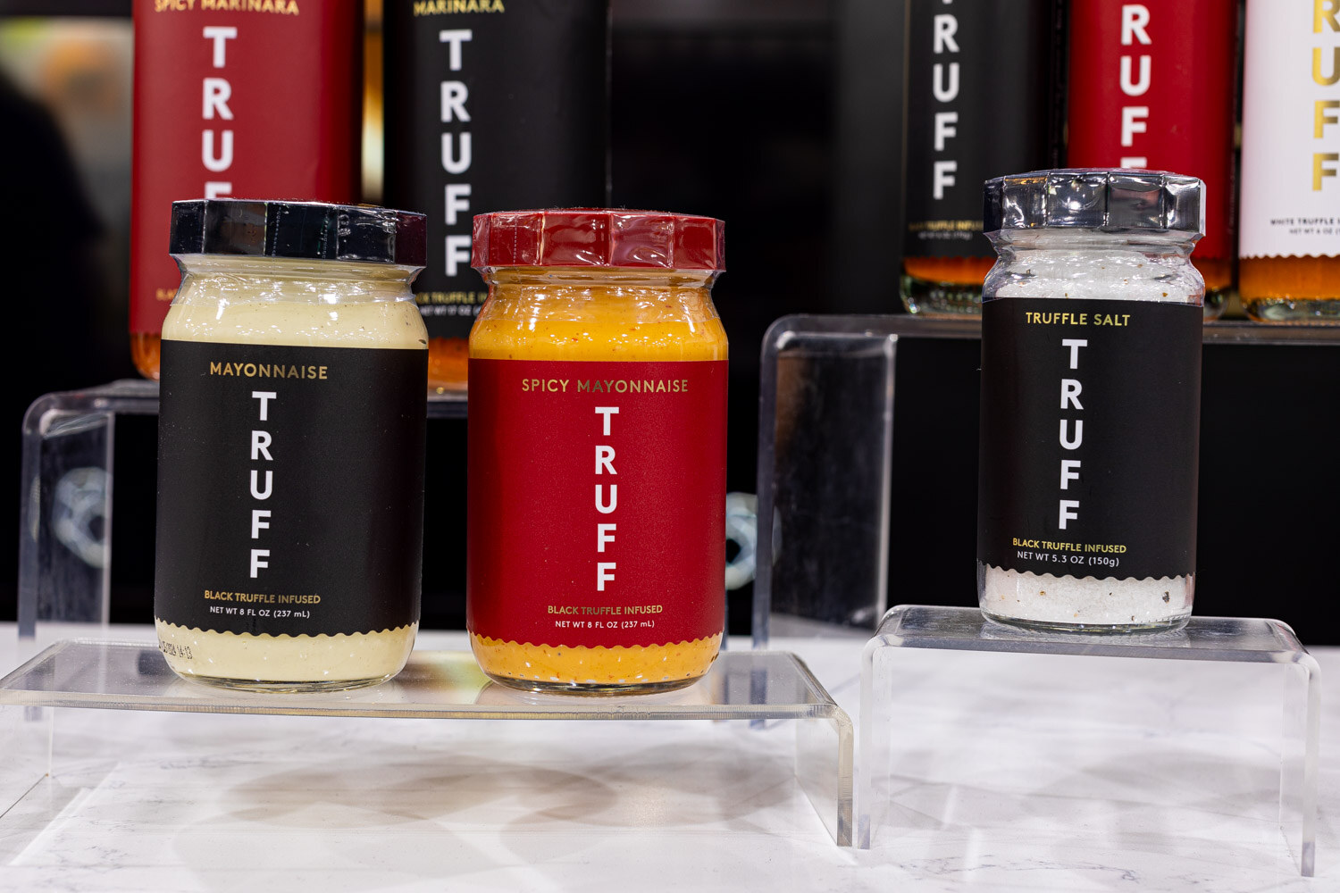 Jars of TRUFF Mayonnaise, Spicy Mayonnaise and Truffle Salt stand on clear acrylic risers in front of black TRUFF bottles