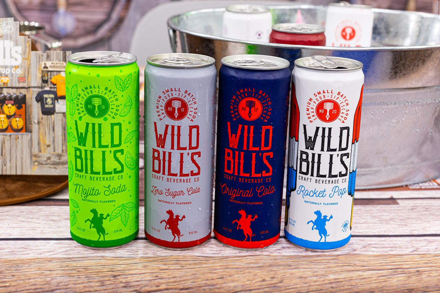 Four tall Wild Bill's cans in Mojito Soda, Zero Sugar Cola, Original Cola and Rocket Pop sit in front of a metal tub