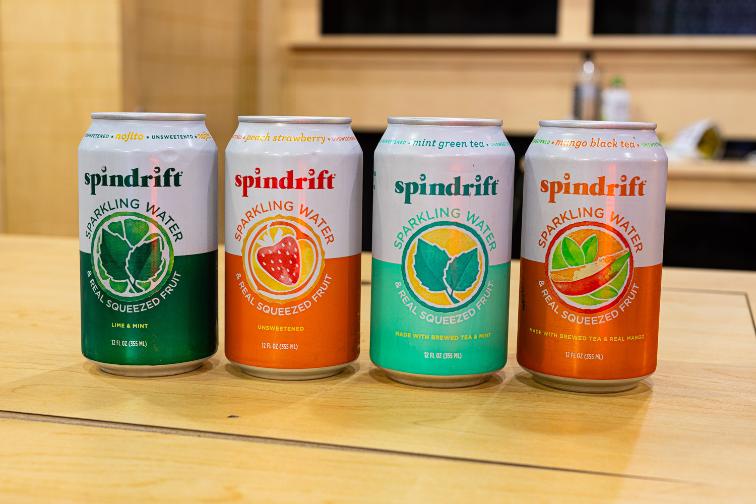 Four Spindrift sparkling water cans in mint, strawberry and lime flavors sit in a row on a light wood counter