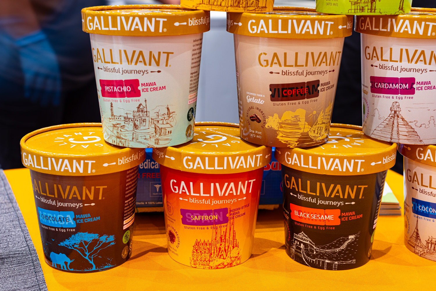 A stack of Gallivant ice cream pints in pistachio and cardamom flavors on a bright yellow table