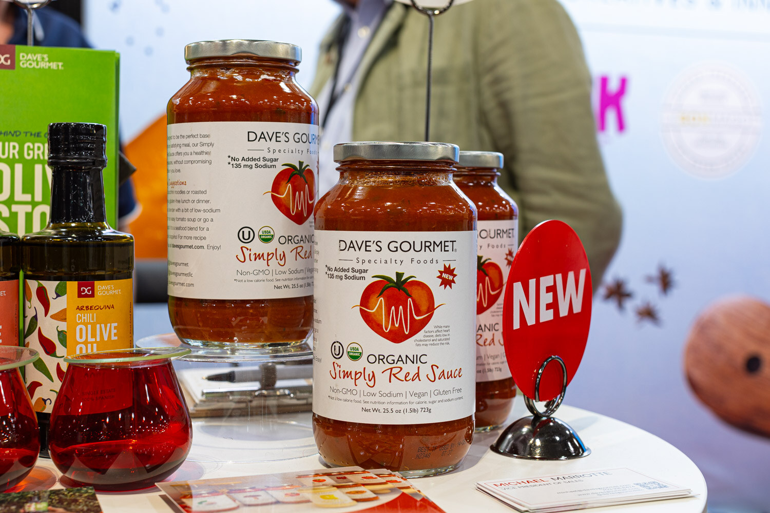 A jar of Dave's Gourmet organic Simply Red sauce with a New tag stands in front of other sauce jars and a bottle of olive oil