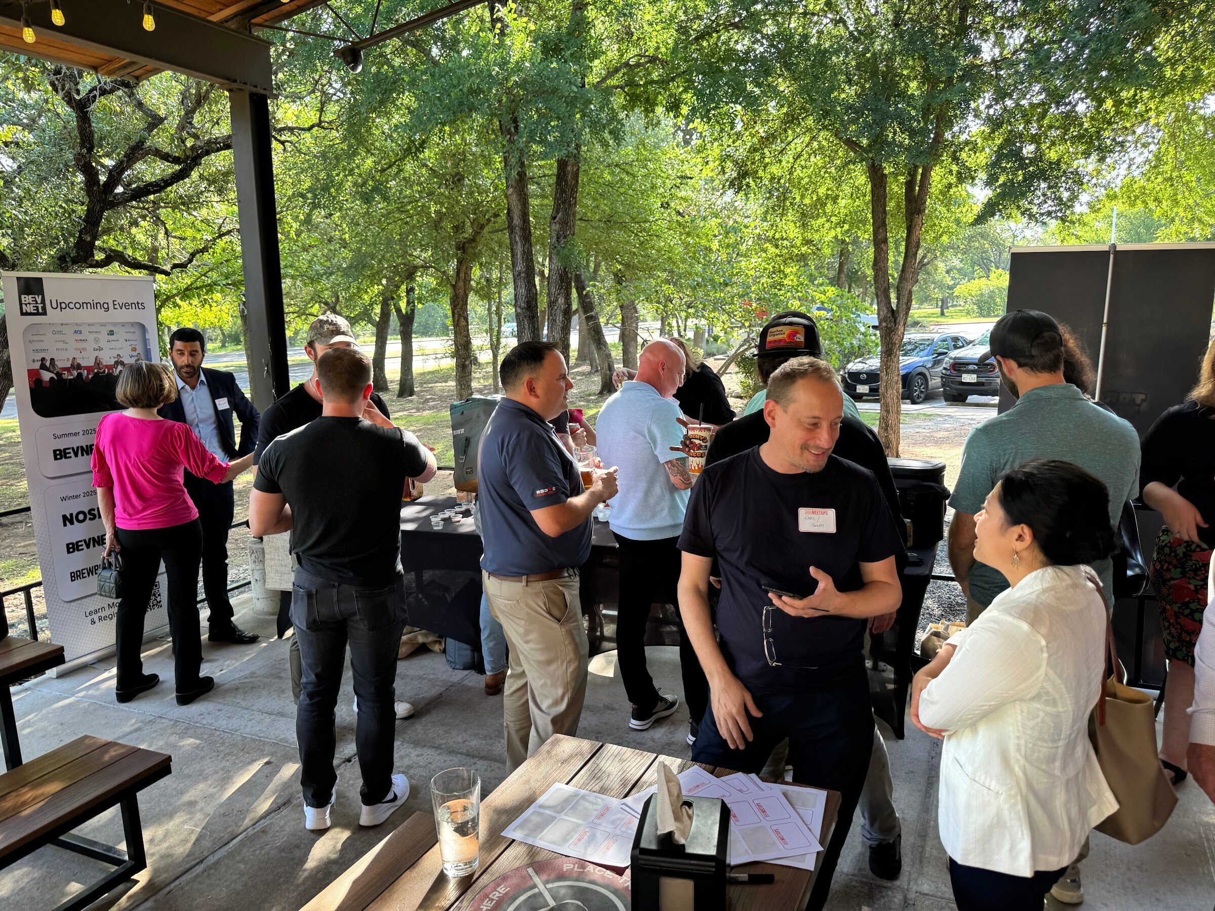 Group of attendees standing and talking on a stone patio next to picnic tables.