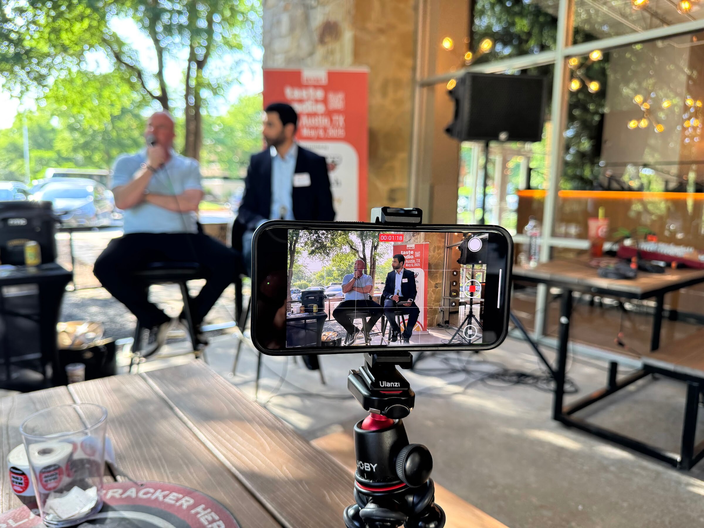 Phone mounted on a tripod filming two seated men in conversation in front of a banner.