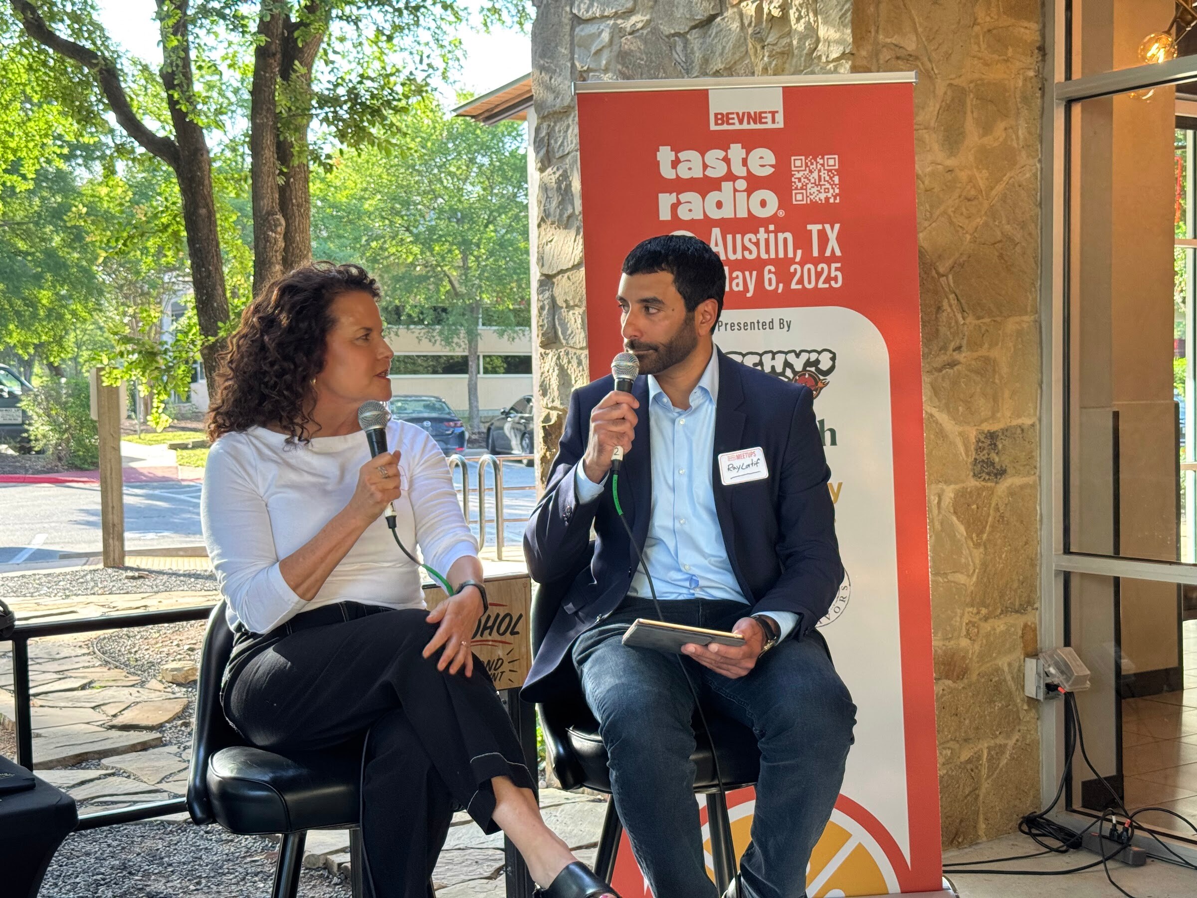 Woman in a white top and black pants seated with the host on stage in front of the Taste Radio banner.