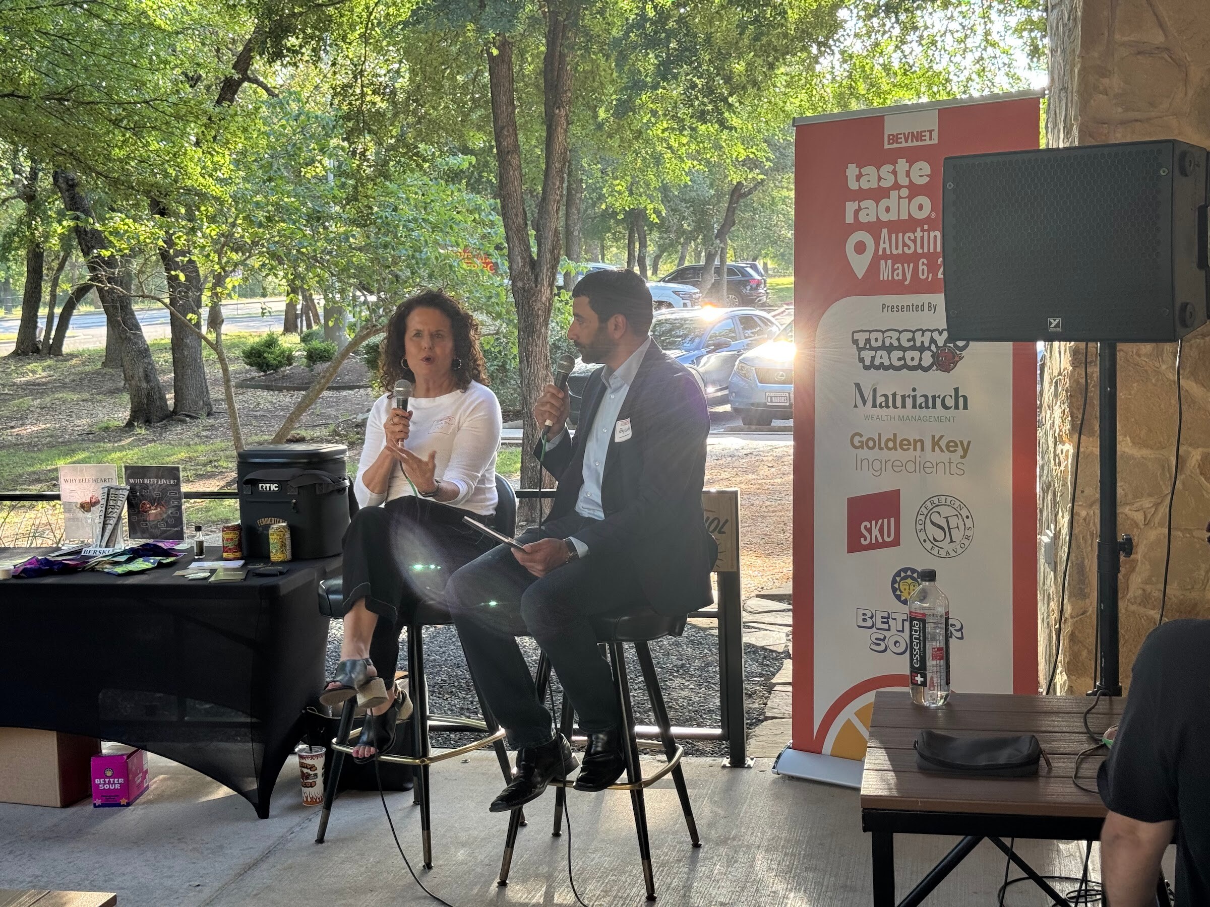 Host and a guest seated on stools beside a banner listing Torchy's Tacos, Matriarch and other partners.