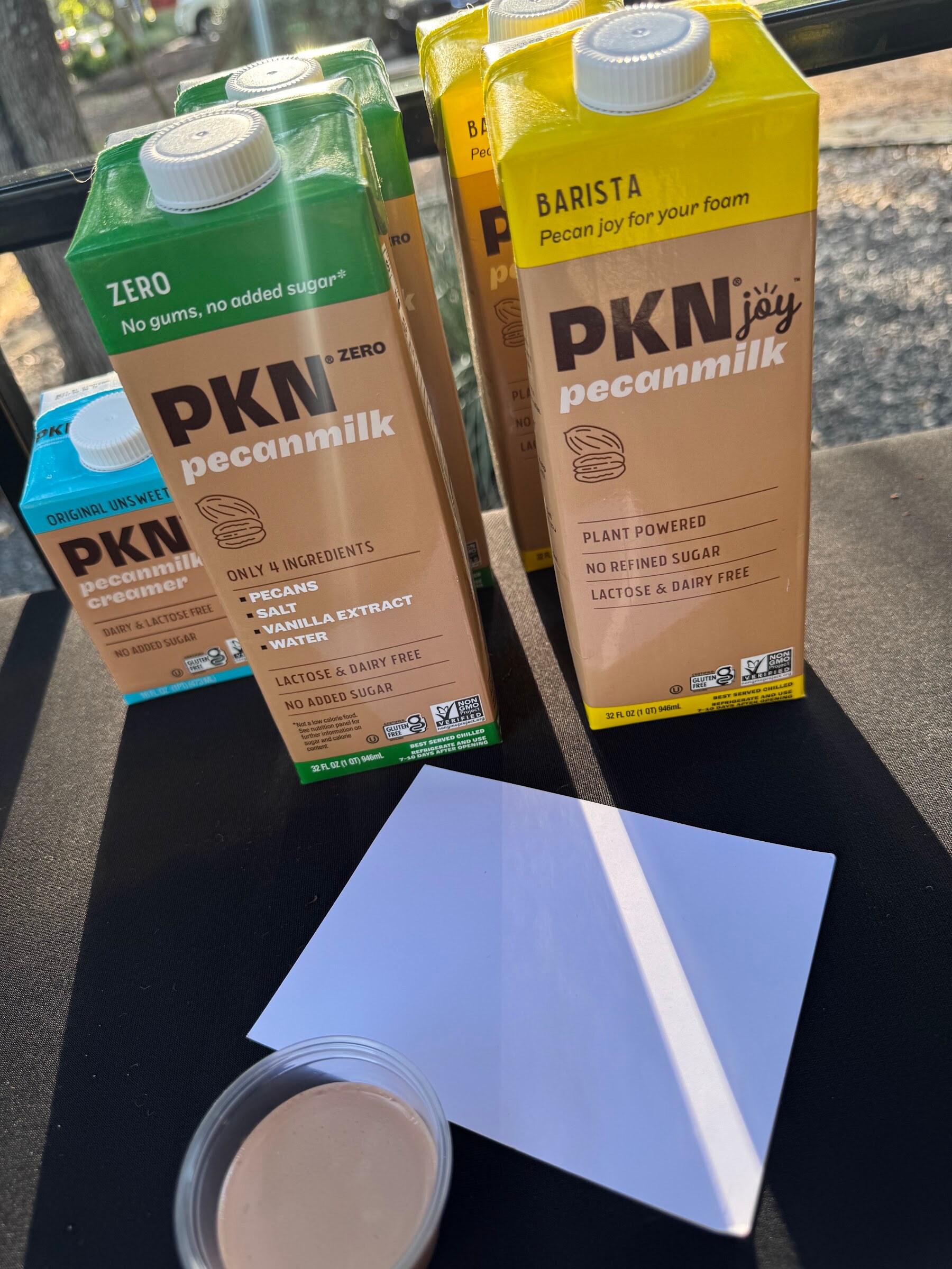 Cartons of PKN pecan milk on a black table with a sample cup.