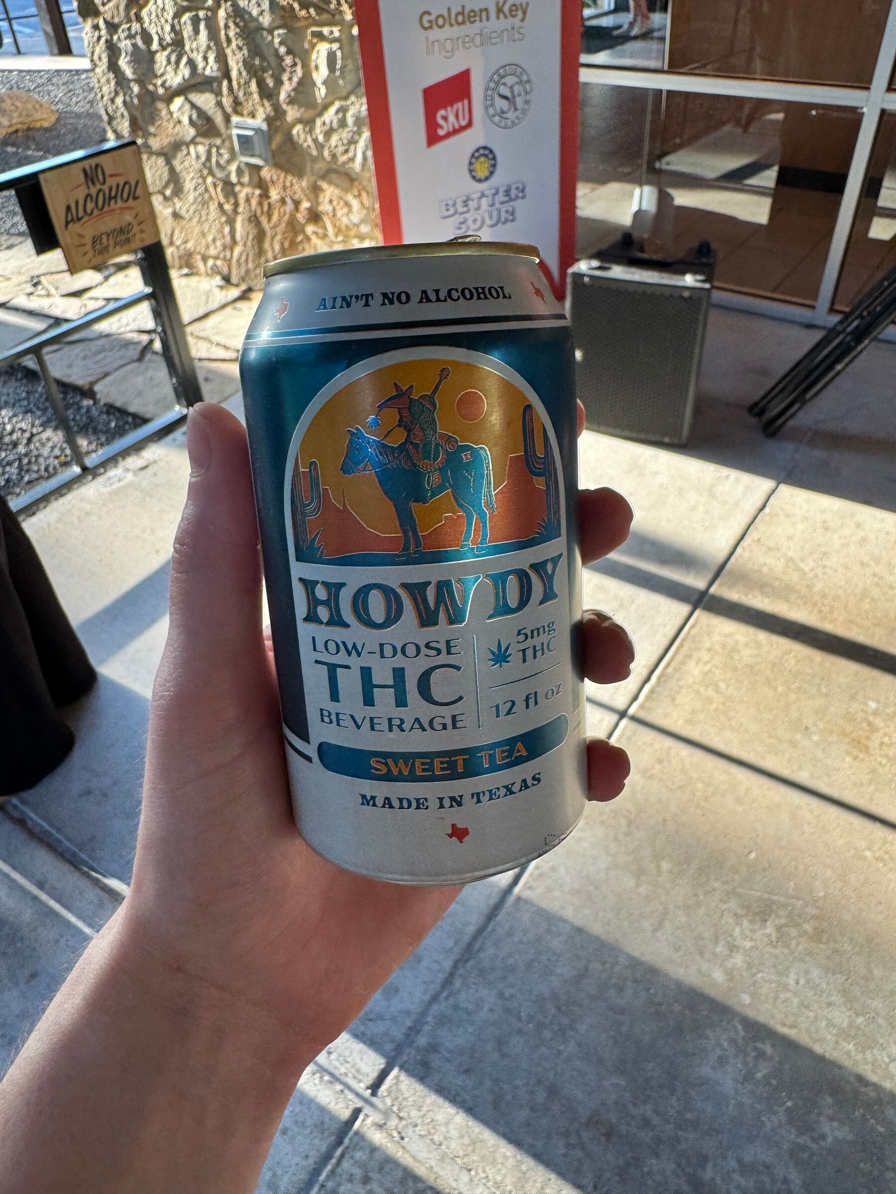 Hand holding a Howdy THC can in front of a patio floor.
