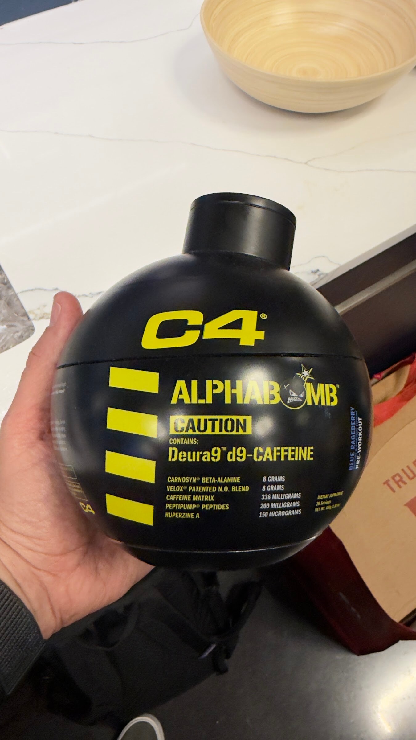 Hand holding a black round C4 Alphabomb bottle with yellow stripes.