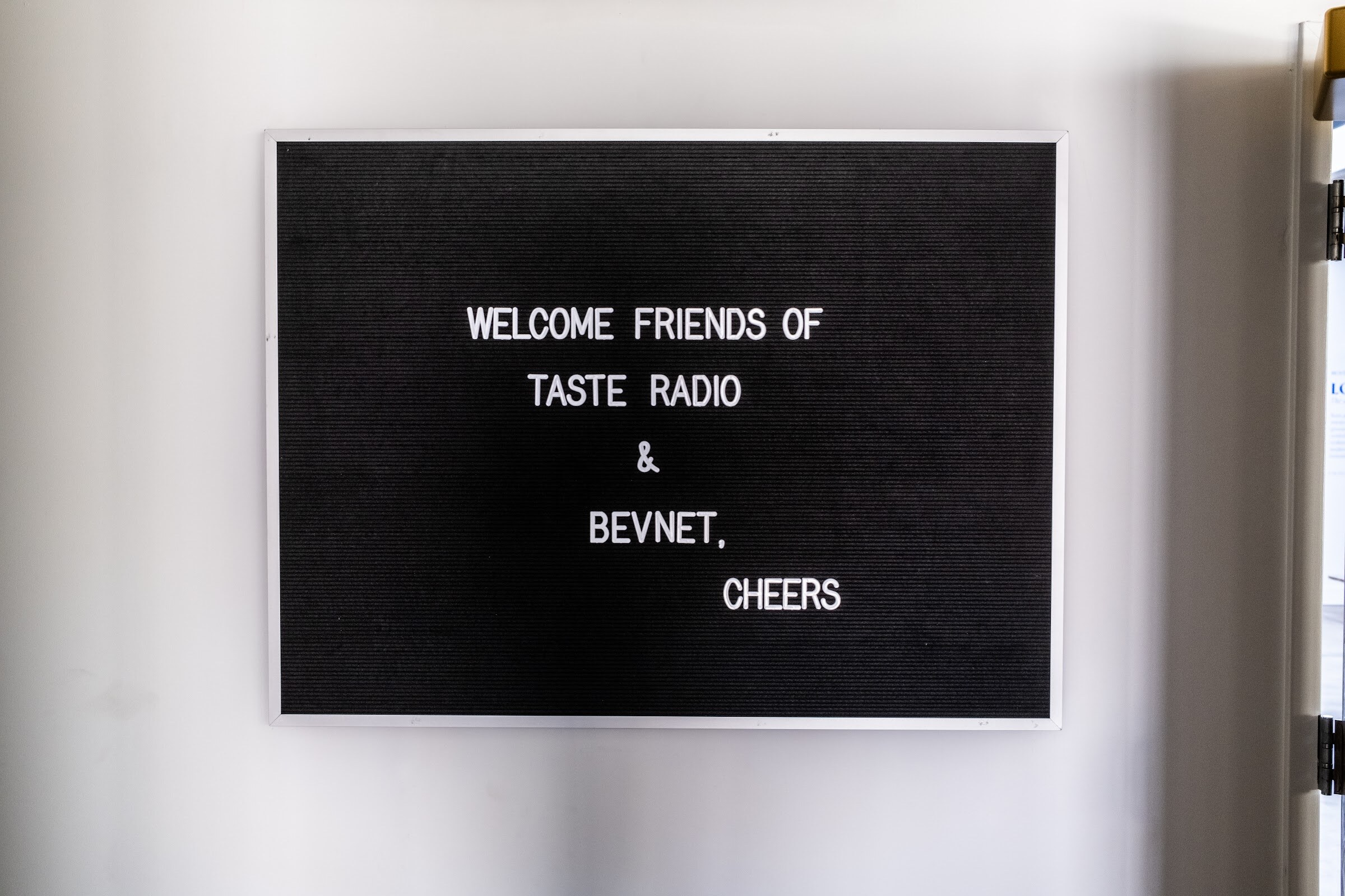 Black letter board reading "Welcome friends of Taste Radio & BevNET, cheers" on a white wall.