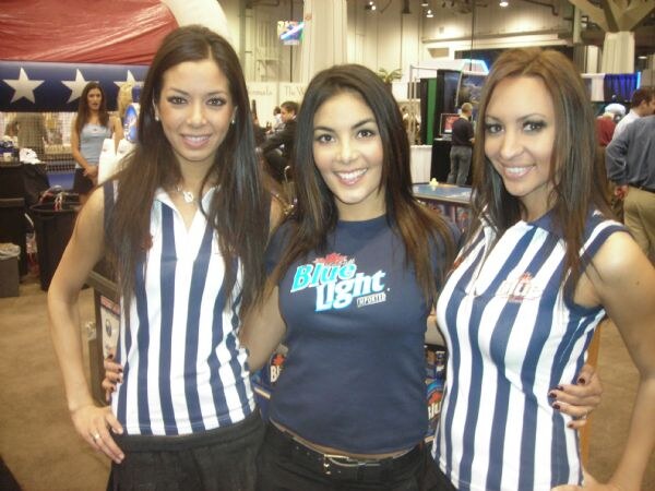 Three smiling women with long dark hair stand together; two wear blue and white striped tops and the one in the middle wears a navy Labatt Blue Light shirt.