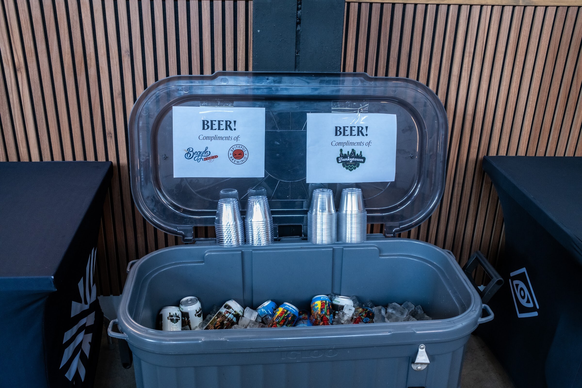 Open gray cooler filled with ice and beer cans, with signs reading "Beer!" on the lid.