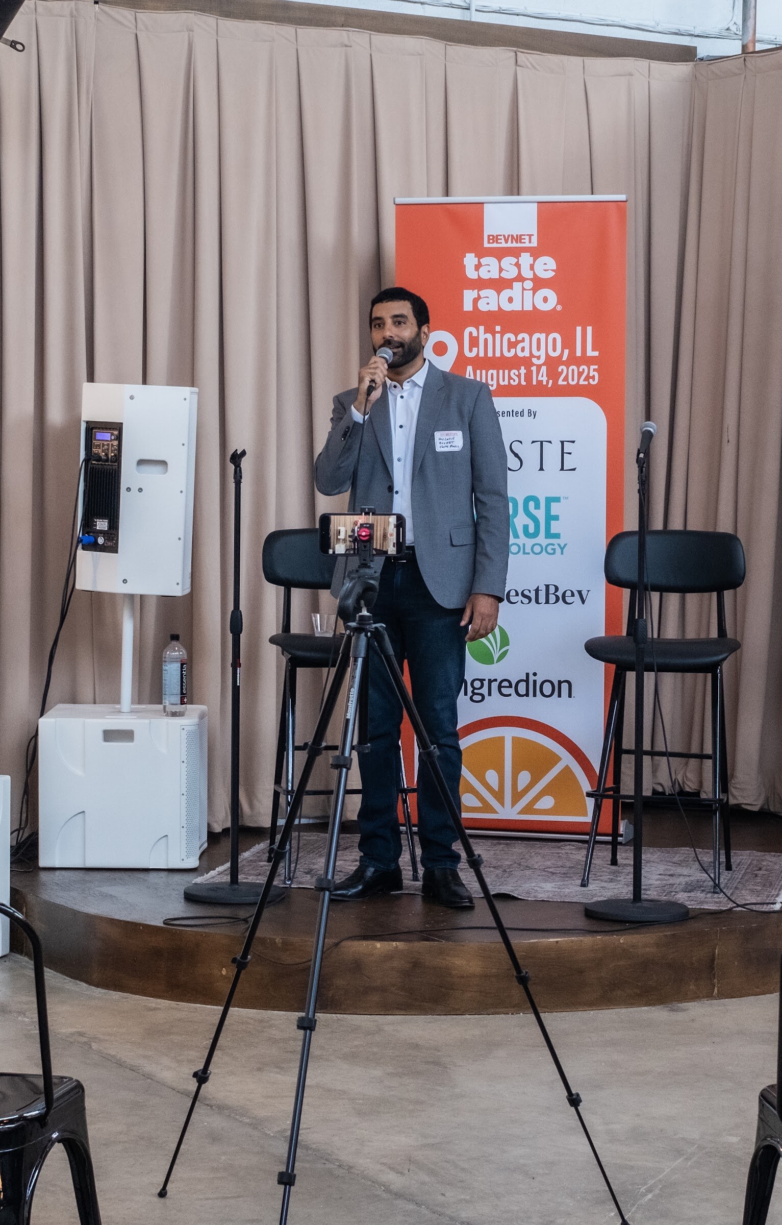 Man in a gray blazer speaking into a microphone in front of an orange Taste Radio Chicago banner.