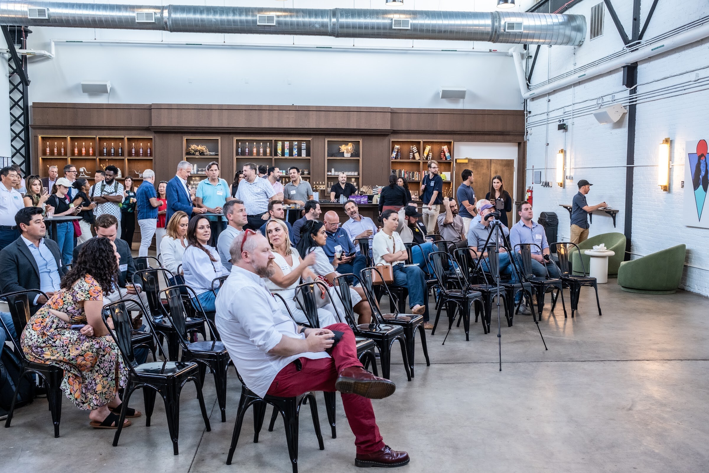Rows of attendees seated in black chairs, with the host speaking at the right edge.