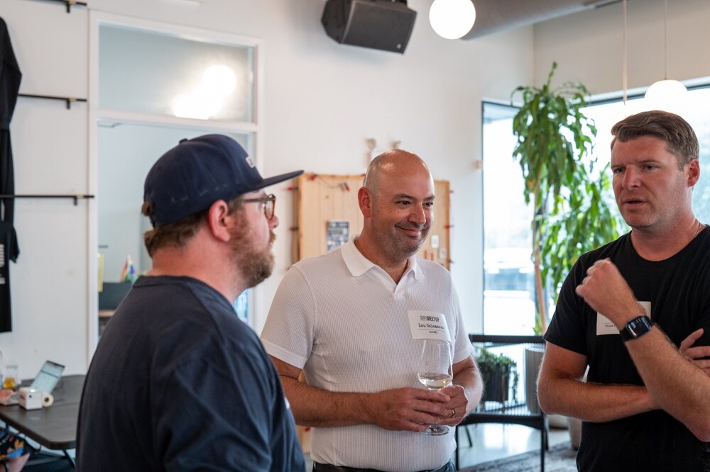 Three men in conversation, one in a white polo holding a wine glass.