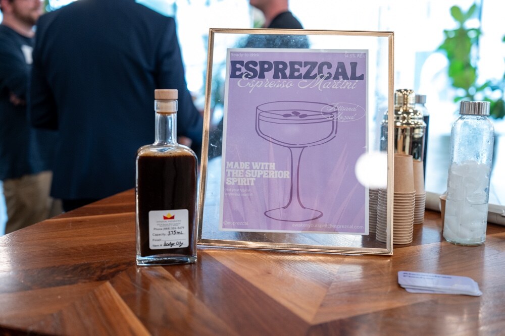 Bottle of Esprezcal beside a framed purple Esprezcal espresso martini sign and a cocktail shaker.