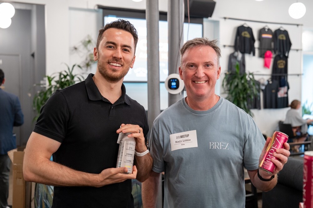 Two smiling men pose holding cans, one in a BREZ t-shirt.