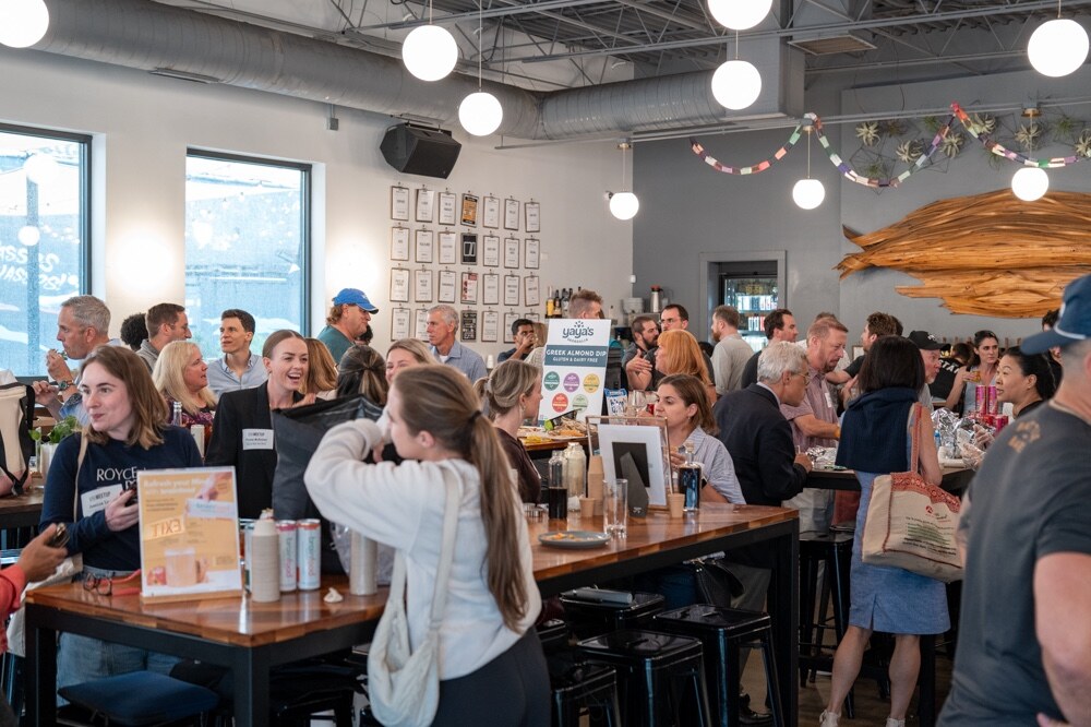 Crowded taproom with attendees at long tables, a carved wood sculpture and paper garlands on the wall.