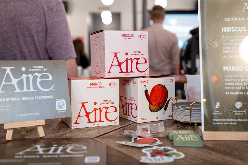 Boxes of Aire Hibiscus and Mango sparkling tonic with an Aire sign on a wooden table.