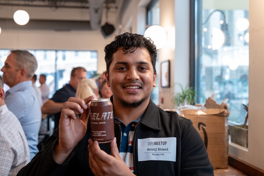 Smiling man in a black jacket holds up a brown can.