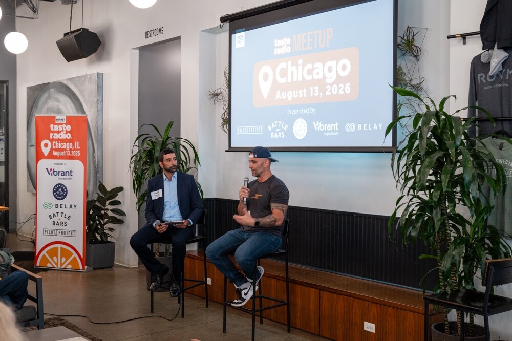 Host in a suit and a guest in a cap and t-shirt sit on stools beside a Taste Radio Chicago banner and screen.