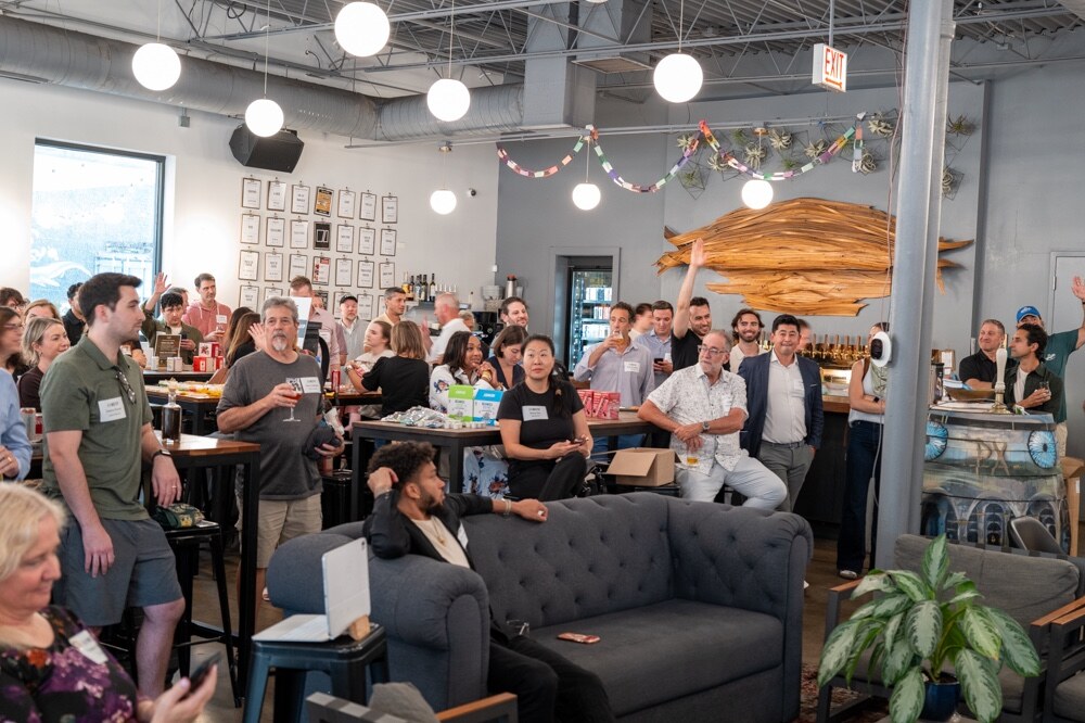 Wide view of a crowd standing and seated around tables and a couch in a taproom.