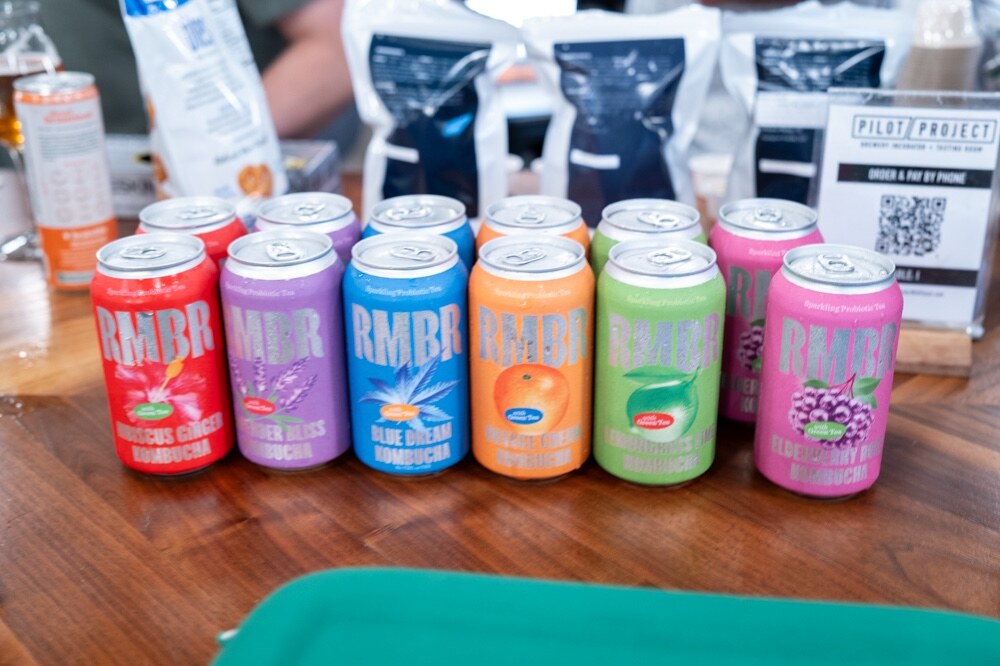 Six colorful cans of RMBR kombucha lined up on a wooden table.
