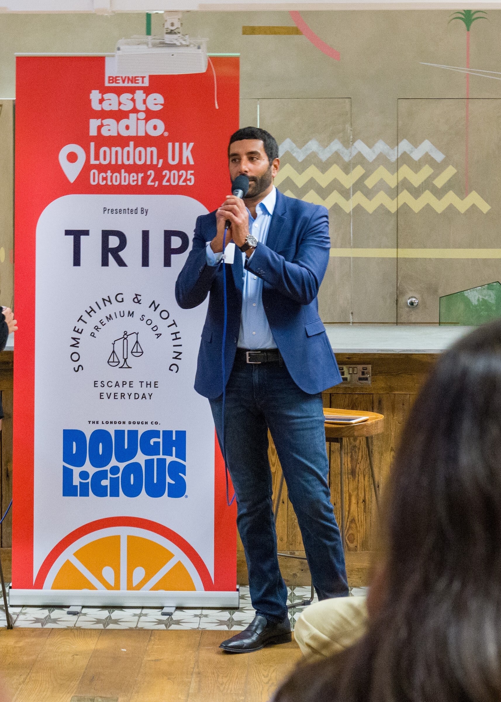 Man in a blue suit speaking into a microphone beside the Taste Radio London banner.
