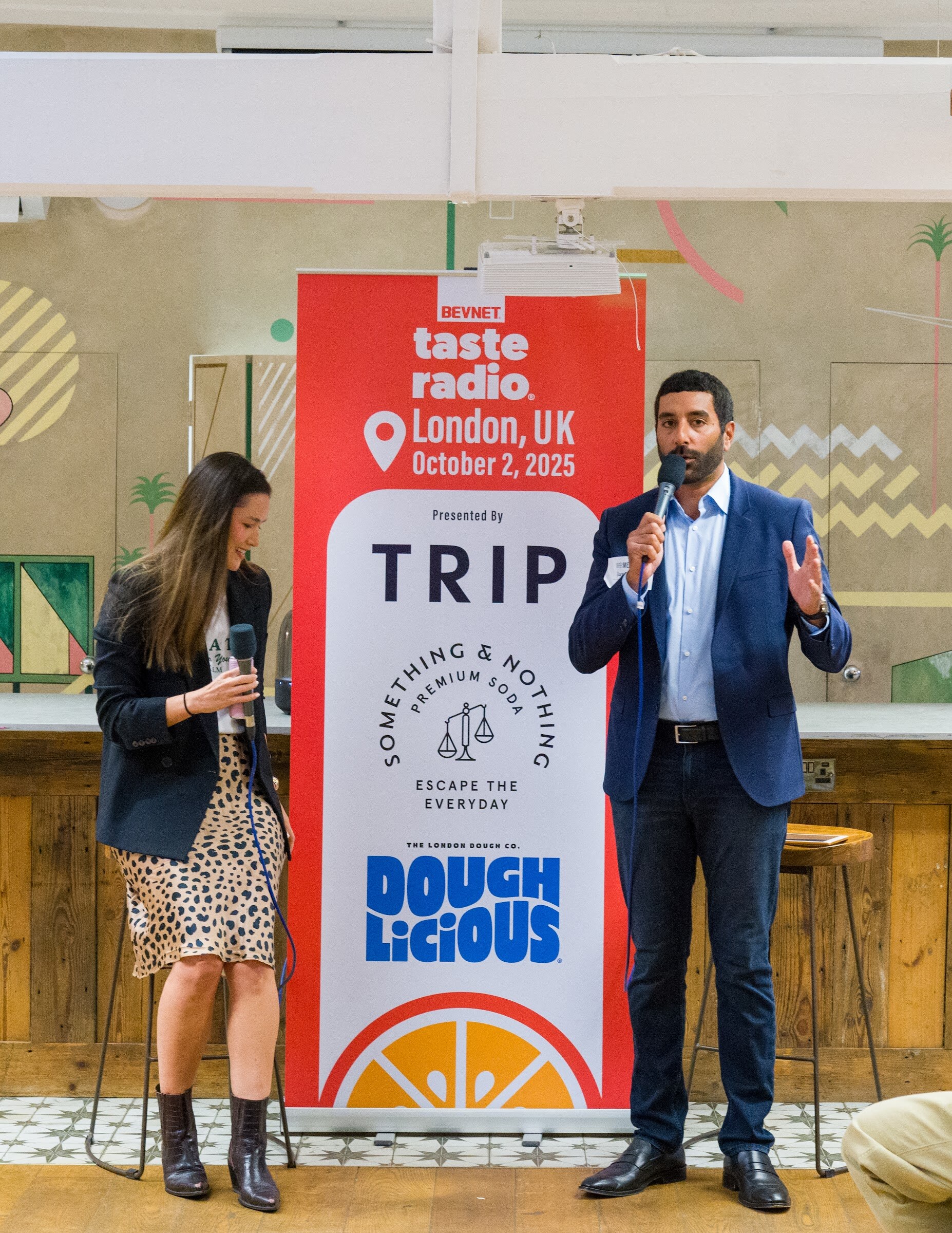Man in a blue suit and woman in a blazer standing beside the TRIP and Doughlicious banner.