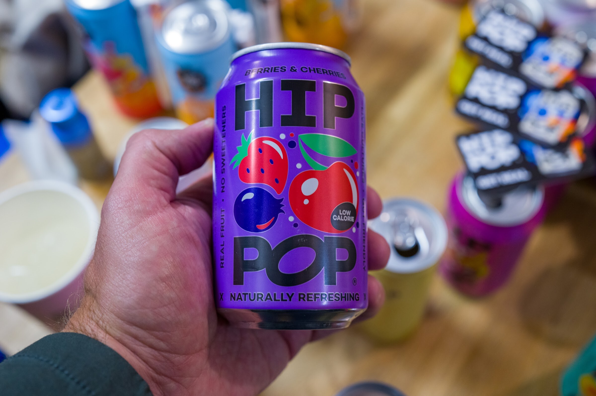 Hand holding a purple Hip Pop can with stickers behind.