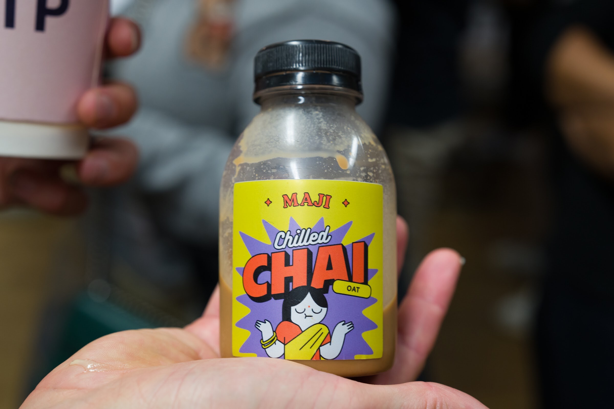 Hand holding a Maji Chilled Chai oat bottle with a yellow and purple label.