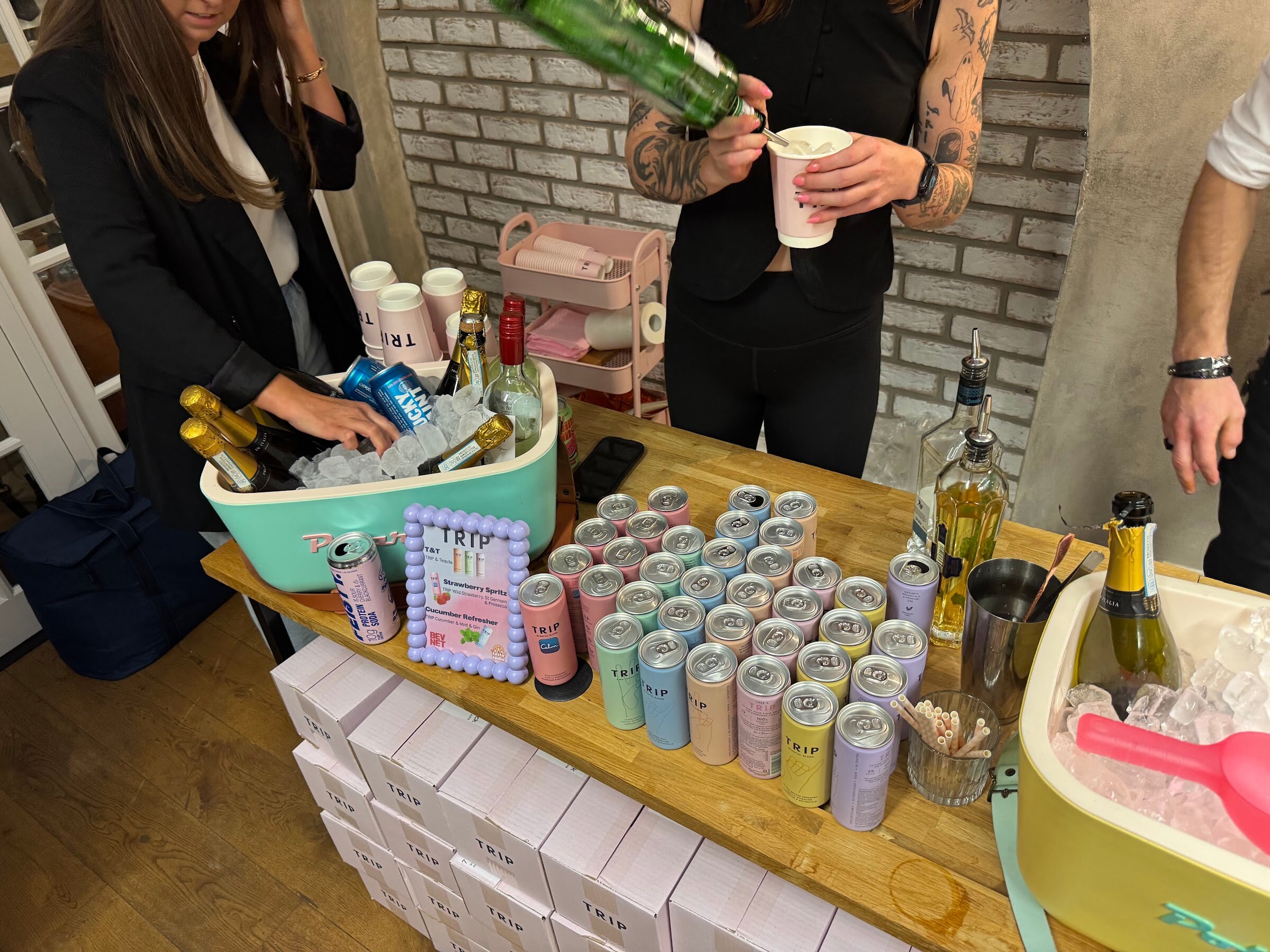 Wooden bar holding rows of TRIP cans and a stand listing flavors, with ice tubs.